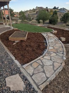 A water conscious landscape design in Fort Collins with a stone patio, mulch beds, gravel, and sod. 