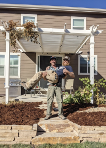 Linden of Linden Leaf Landscapes posing holding up his client in front of a retaining wall project in Fort Collins