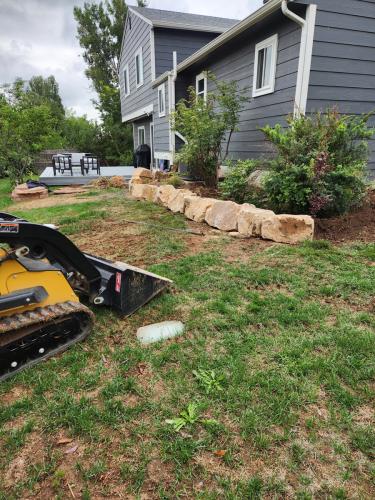 Skid steer moving large rocks to create planter beds in Colorado