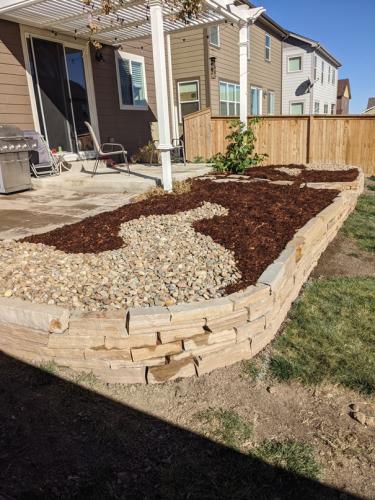 Raised stone landscape bed design with pebble pathway and mulch