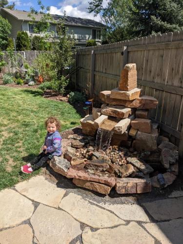 A toddler sitting by a custom water feature hardscape in Fort Colllins